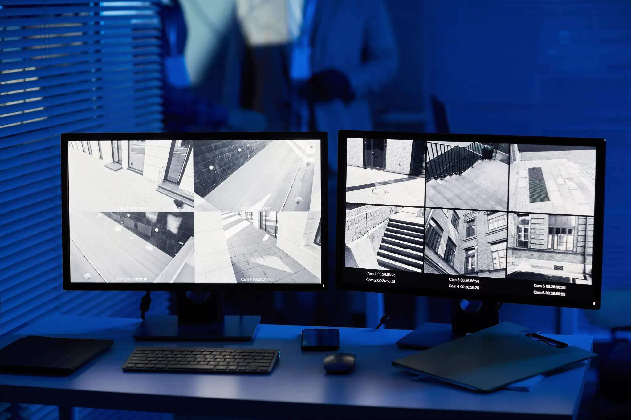 Security monitoring system with surveillance camera feeds on dual monitors in blue-lit room